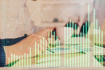 Double exposure of man's hands writing notes of stock market with forex graph.