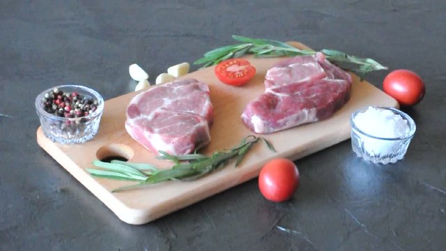 Two raw pork steaks with tomato, rosemary, spices and garlic on a cutting board