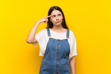 Young woman in dungarees over isolated yellow background making the gesture of madness putting...