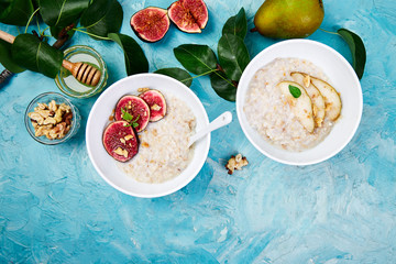 Healthy breakfast. A bowls  of porridge with pears slices and walnuts and porridge with figs on blue background. Two bowls. Flat lay. Copy space. Top view.