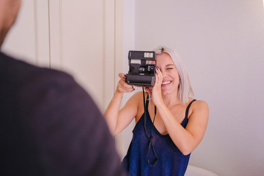 Couple taking pictures at home. Capture and learning photography concept. Young woman shooting a photo with modern instant camera. Trendy girl taking snapshots to boyfriend at home.