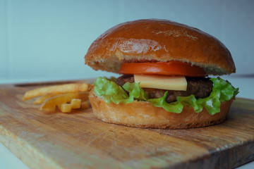 A traditional American burger with a chop, tomato and cheese on a salad leaf. French fries. fast food.