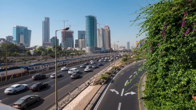 A timelapse of road traffic on the Ayalon Highway (Israel). Cars are not blurred but fully visible. Tall buildings in the distance, over a clean sky.