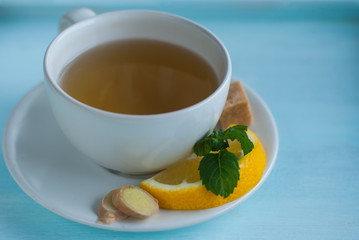 white cup of green tea with lemon, ginger, mint and brown sugar on the blue wooden table