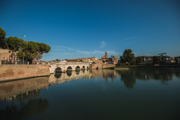 Fototapeta premium Rimini, Italy - September 11, 2019: Tiberius bridge in Rimini on a background of blue sky with white clouds