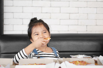 Asian child cute or kid girl enjoy eating hawaiian pizza or italian food in box with thick cheese and crisp thin to hungry for happy breakfast or lunch at cafe restaurant or home on table and sofa