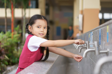 Asian child cute or kid girl and student smiling happy with wash hands on tap in sink on public at kindergarten school or preschool for dirty clean and bacteria or virus with wear school uniform