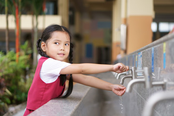 Asian child cute or kid girl and student smiling happy with wash hands on tap in sink on public at kindergarten school or preschool for dirty clean and bacteria or virus with wear school uniform