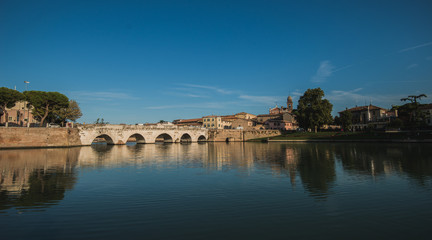 Fototapeta premium Rimini, Italy - September 11, 2019: Tiberius bridge in Rimini on a background of blue sky with white clouds