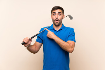 Young handsome golfer man over isolated background surprised and pointing side