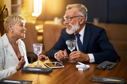 Man in elegant tuxedo and woman in white clothes use tablet pc. Man holding tablet in hand. speak, chat with each other - Powered by Adobe