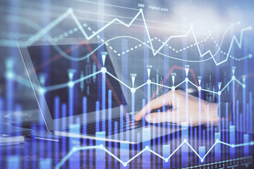 Double exposure of businessman's hands with laptop and stock market graph background. Concept of research and trading.