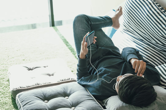 asian teenager man listening to music from smart mobile phone while lying on floor at home