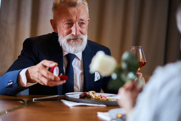 Caucasian gray-haired man in tuxedo offers to get married. Lovely face of male. Woman keep white rose in hands