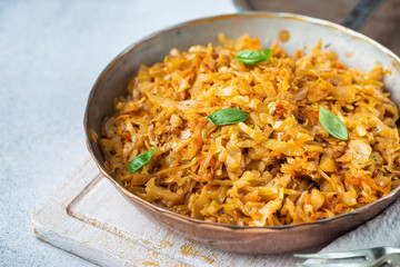 Stewed or braised cabbage served in a frying pan on light stone background, close up