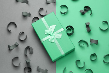soft green gift box with festive bow top view on a gray and mint background with paper confetti