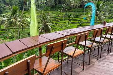 Wooden table and chairs in empty tropical cafe next to rice terraces in island Bali, Indonesia