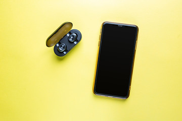 Mobile phone with wireless headphones isolated on yellow background - close-up view