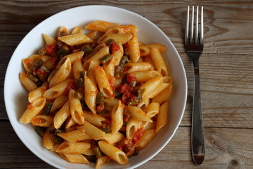 Piatto di pasta condita con pomodoro e fagiolini su fondale di legno.