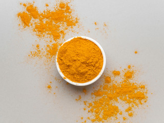 Turmeric powder. Traditional indian golden healthy spice in white ceramic bowl on gray background....