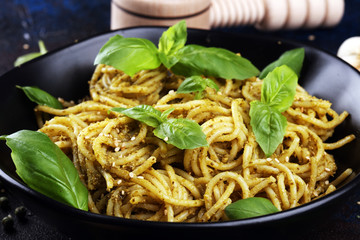 Plate of delicious spaghetti pesto garnished with parmesan cheese and basil on rustic dark background