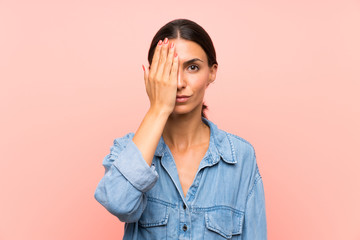 Young woman over isolated pink background covering a eye by hand