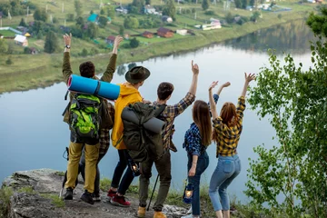 Tuinposter Young ambitious people with backpacks standing with raised hands on top of a mountain and enjoying valley view, happiness © alfa27