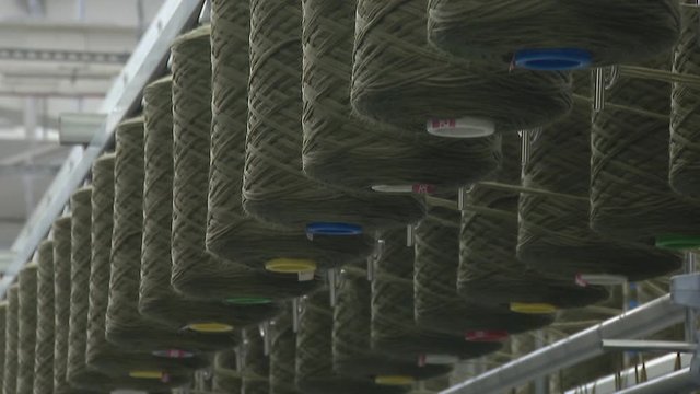 Factory for the production of clothing fabrics. Large spools of thread feed the carpet.