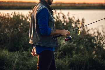 Caucasian adult bearded men stand near lake and fish. Sunset.