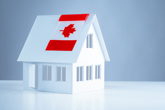 Model Cottage With The Flag Of Canada. Acquisition Of Real Estate In Canada. Moving To Ottawa. Real Estate Prices Abroad. Moving To Another Country.