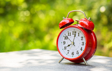 Morning concept. Alarm clock closeup. Red alarm clock on garden table with natural lights background, outdoors