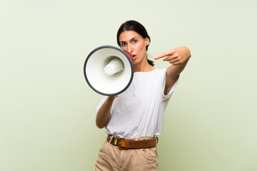 Young woman over isolated green background shouting through a megaphone