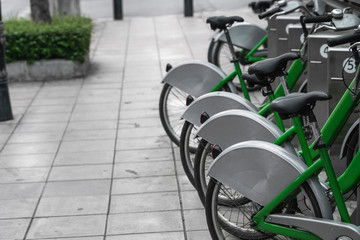 Street transportation green hybrid rent bicycles with electronic form of payment for traveling around the city stand in row on rental network parking lot waiting for cyclists to make bike trip.
