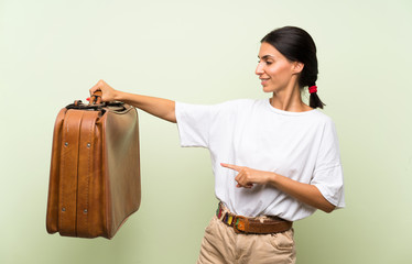 Young woman over isolated green background holding a vintage briefcase