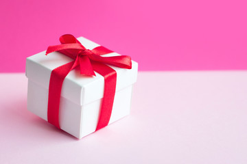 White box with a red ribbon on a light pink background, copy space. Greeting card concept. Sale concept