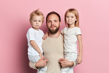 handsome father carrying his little daughter and son on pink background, happy fatherhood,...