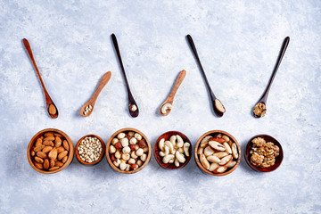 pecans, hazelnuts, almonds, pine nuts, Brazil nut, cashews in wooden bowls on blue background, top...
