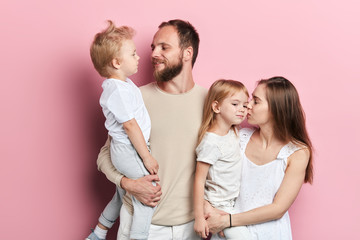 young daddy and mommy kissing their kids, close up portrait, isolated pnk background, love, positive feeling and emotion
