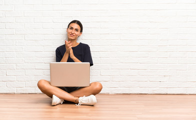 Young woman with a laptop sitting on the floor applauding