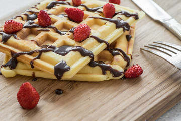 Two Viennese waffles with chocolate and berries on a wooden Board