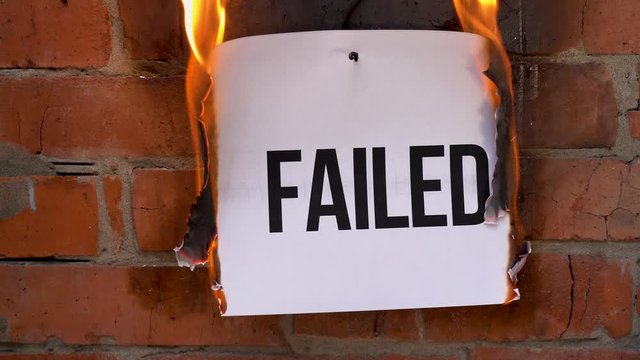 The inscription on a white A4 size sheet against the background of an orange brick wall. The paper with the black word Failed burns, smoke and turns into ashes. Business concept.