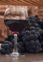 A glass of fragrant red wine and bunches of blue grapes