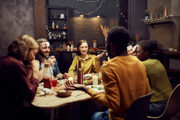 Group of young friends playing guessing game while sitting at table during dinner party in dark room, copy space