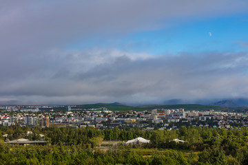 A cityscape of Reykjavík, the capital and largest city of Iceland, photographed from a hill on a cloudy summer day.