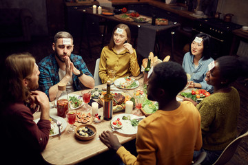 High angle view at group of friends playing guessing game while sitting at table enjoying dinner party in dark room, copy space
