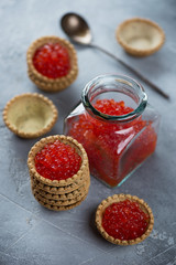 Glass jar with red caviar and tartlets over grey concrete background, vertical shot, selective focus