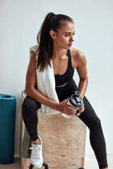 Long-haired fitness female in sportswear sit with plastic bottle after fitness. Have rest, tired....