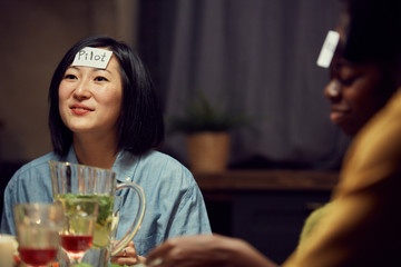Portrait of smiling Asian woman playing guessing game with friends during party, pilot sticker on her forehead