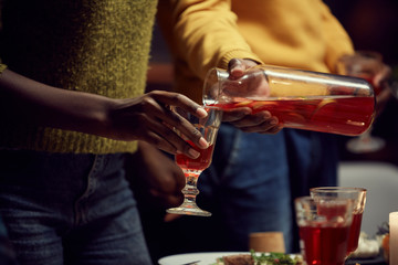 Close up of African-American woman pouring raspberry lemonade into glass while standing at dinner table during party, copy space