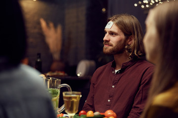Side view portrait of bearded young man playing guessing game with friends during party in dark room, copy space
